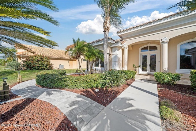 entrance to property featuring a tiled roof, french doors, and stucco siding