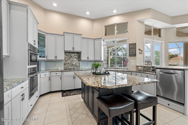 kitchen with light tile patterned floors, stainless steel appliances, decorative backsplash, a kitchen island, and a sink