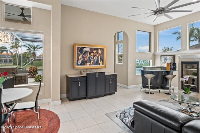 living room featuring arched walkways, light tile patterned floors, a towering ceiling, a ceiling fan, and baseboards