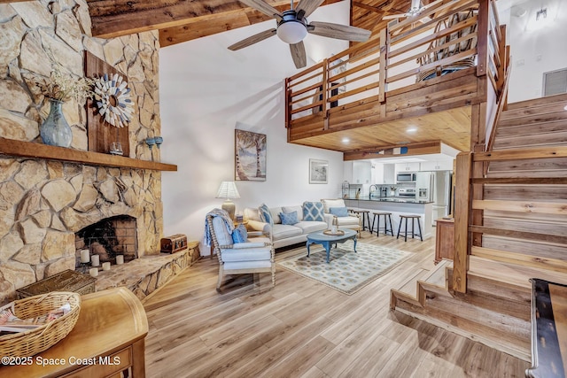 living room featuring beam ceiling, ceiling fan, a stone fireplace, high vaulted ceiling, and light hardwood / wood-style floors