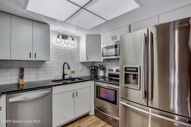 kitchen with sink, dark stone countertops, light wood-type flooring, tasteful backsplash, and stainless steel appliances