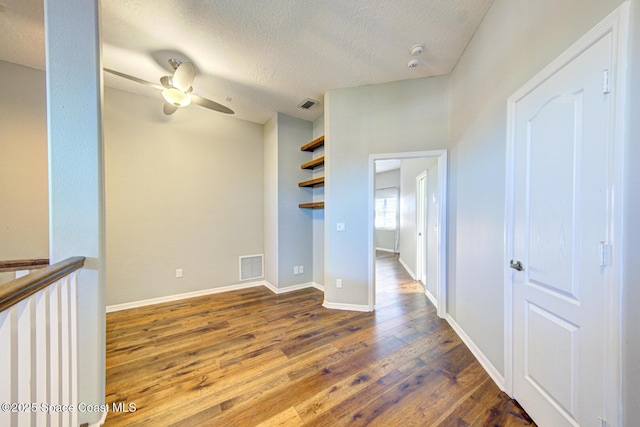 empty room with a textured ceiling, ceiling fan, and dark hardwood / wood-style floors