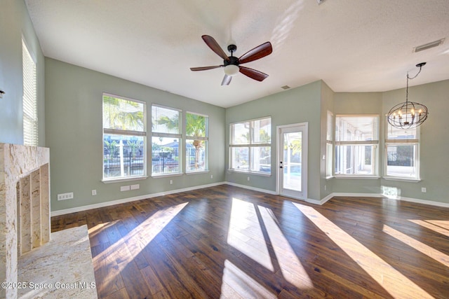 unfurnished living room with a textured ceiling, ceiling fan with notable chandelier, a wealth of natural light, and dark wood-type flooring