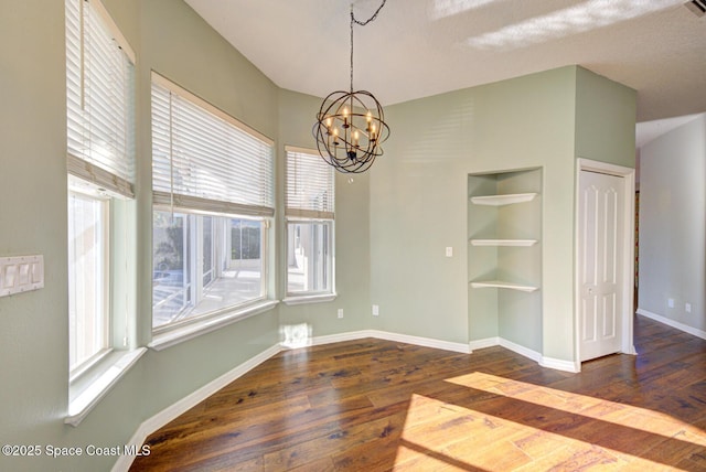 unfurnished dining area with built in features, a chandelier, and dark hardwood / wood-style floors