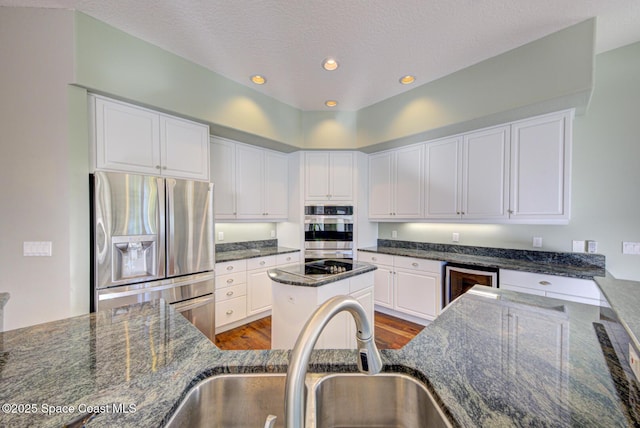 kitchen with appliances with stainless steel finishes, beverage cooler, sink, dark stone countertops, and white cabinetry