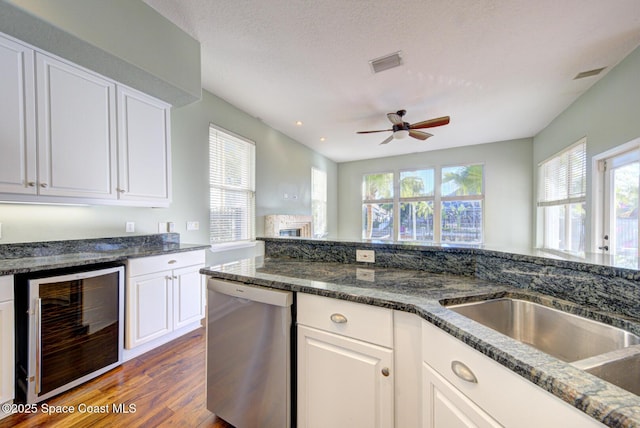 kitchen featuring stainless steel dishwasher, white cabinetry, beverage cooler, and dark stone counters