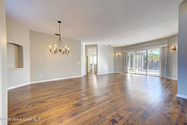 empty room with a textured ceiling, a notable chandelier, and dark wood-type flooring