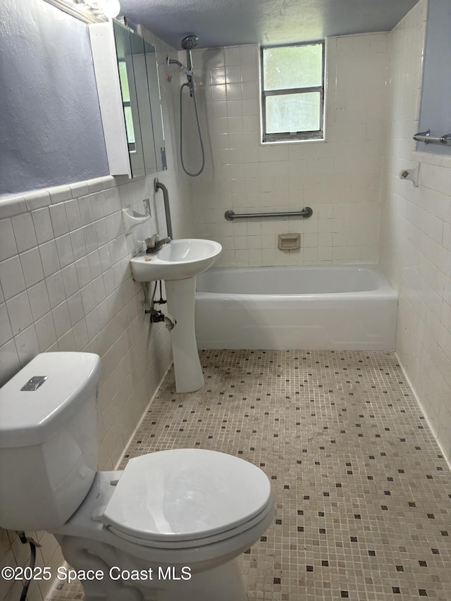 bathroom featuring tile patterned flooring, tiled shower / bath combo, toilet, and tile walls