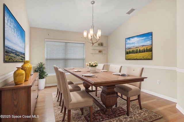 dining area with light hardwood / wood-style flooring, a notable chandelier, and vaulted ceiling