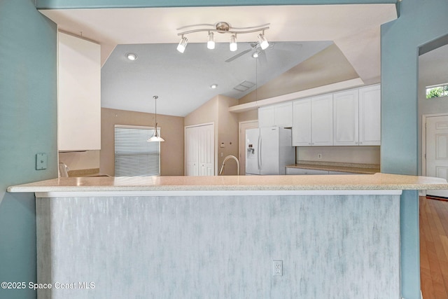 kitchen with lofted ceiling, decorative light fixtures, kitchen peninsula, white fridge with ice dispenser, and white cabinets