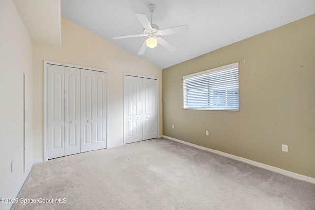 unfurnished bedroom with multiple closets, vaulted ceiling, light colored carpet, and ceiling fan