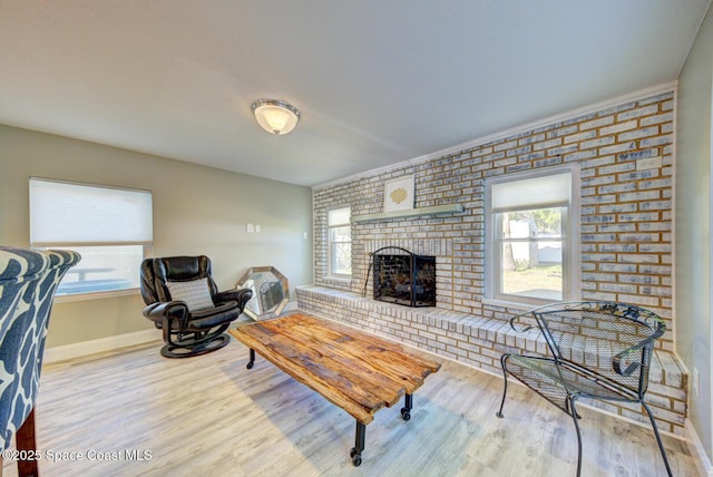 living room featuring light wood-type flooring, brick wall, and a brick fireplace