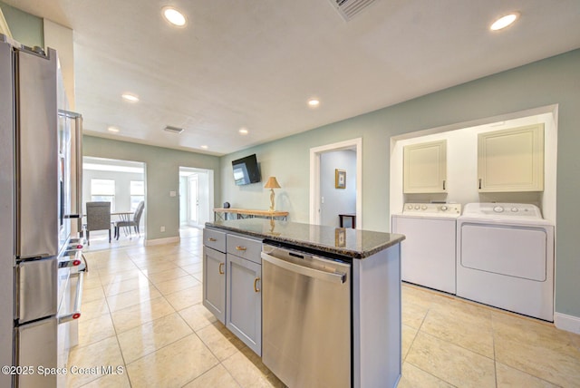 kitchen with gray cabinetry, stainless steel appliances, separate washer and dryer, dark stone counters, and a kitchen island