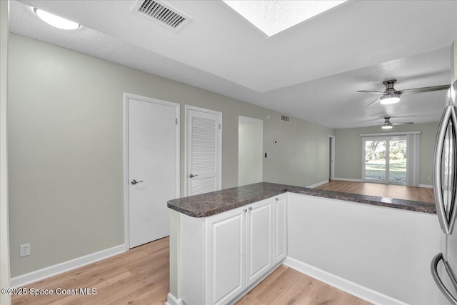 kitchen with kitchen peninsula, a textured ceiling, ceiling fan, white cabinetry, and stainless steel refrigerator