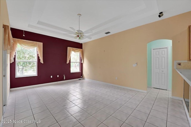 unfurnished room featuring a tray ceiling, ceiling fan, light tile patterned floors, and a healthy amount of sunlight