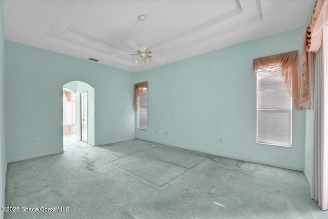 carpeted spare room with ceiling fan, a wealth of natural light, and a tray ceiling