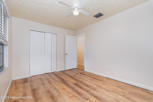 unfurnished bedroom with ceiling fan, a closet, light hardwood / wood-style floors, and a textured ceiling