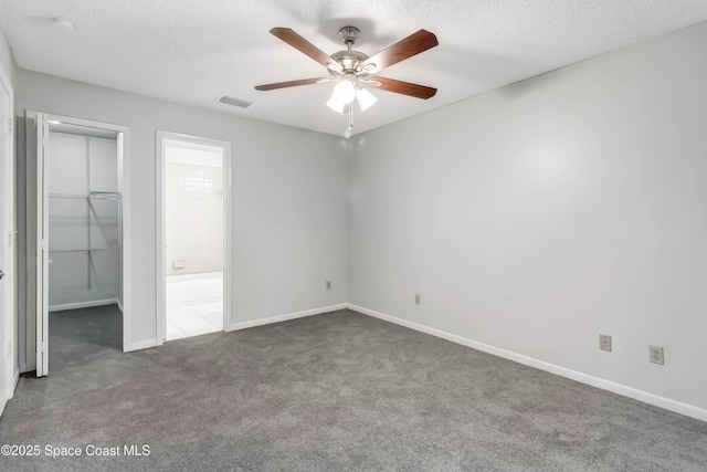 unfurnished bedroom featuring a textured ceiling, a walk in closet, dark carpet, a closet, and ceiling fan