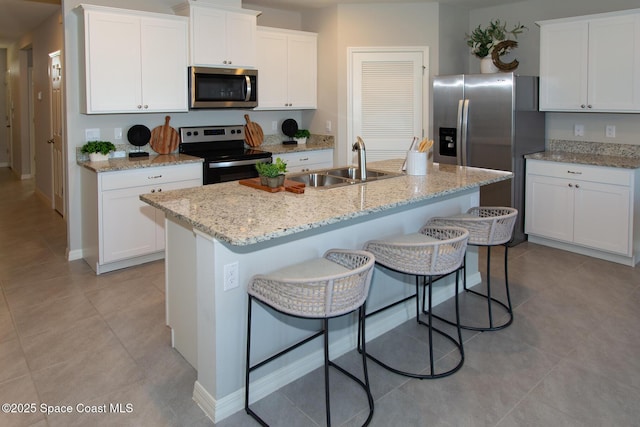 kitchen featuring white cabinets, appliances with stainless steel finishes, a kitchen island with sink, and a breakfast bar area