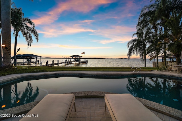 pool at dusk featuring a boat dock and a water view