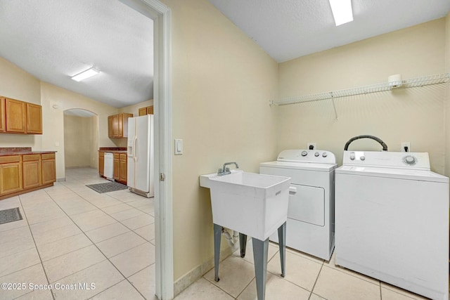 washroom featuring washing machine and dryer, sink, light tile patterned floors, and a textured ceiling