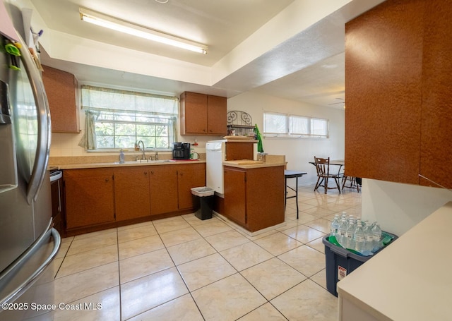 kitchen with a healthy amount of sunlight, kitchen peninsula, stainless steel refrigerator, and a tray ceiling