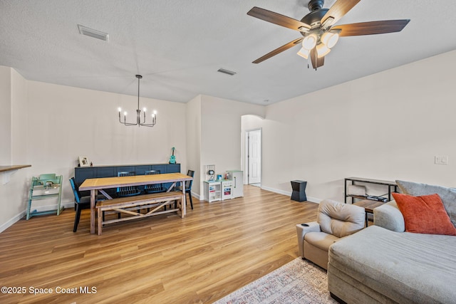 living room with a textured ceiling, light wood-type flooring, and ceiling fan with notable chandelier