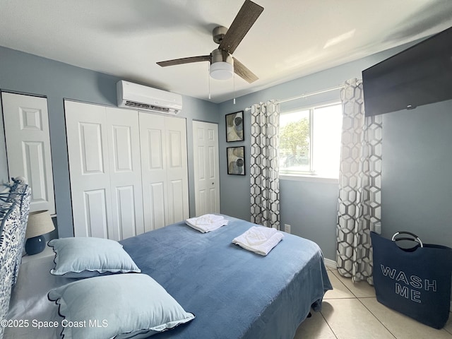 bedroom featuring light tile patterned floors, multiple closets, a ceiling fan, a wall mounted air conditioner, and baseboards