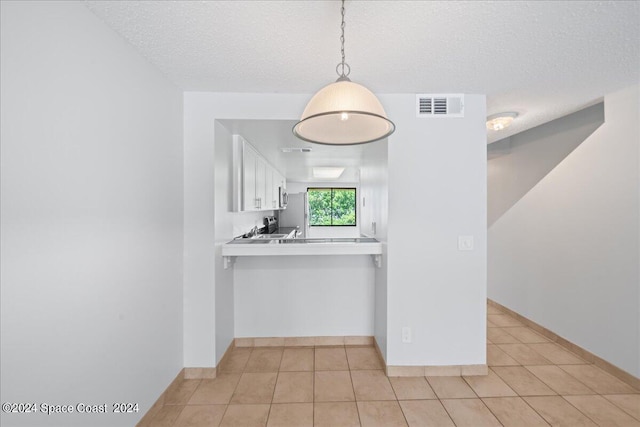 kitchen featuring a textured ceiling, white cabinetry, light tile patterned flooring, and decorative light fixtures