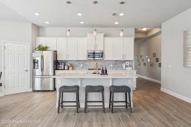 kitchen with white cabinetry, an island with sink, light wood-type flooring, and appliances with stainless steel finishes