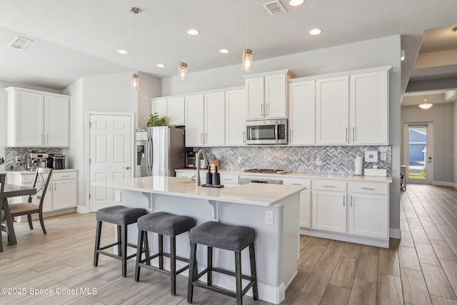 kitchen with white cabinets, hanging light fixtures, an island with sink, and appliances with stainless steel finishes