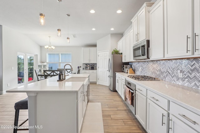 kitchen with white cabinetry, a kitchen island with sink, hanging light fixtures, and stainless steel appliances