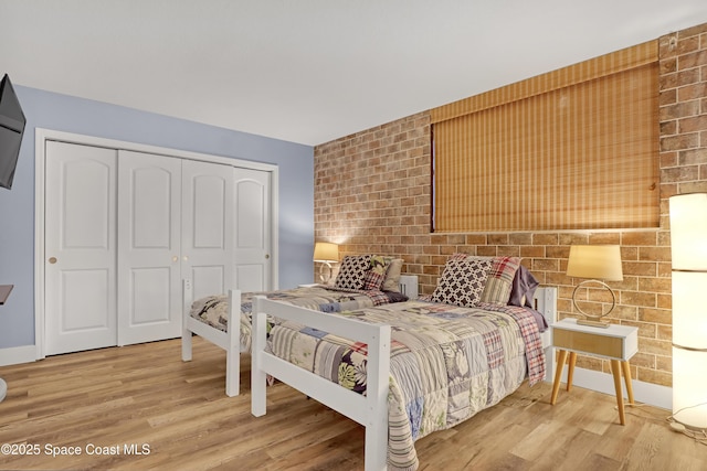 bedroom featuring a closet, wood-type flooring, brick wall, and white refrigerator