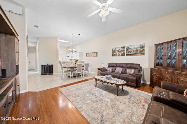 living room with a textured ceiling, ceiling fan with notable chandelier, and light hardwood / wood-style flooring