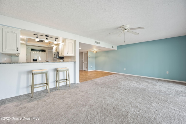 unfurnished living room featuring ceiling fan, a textured ceiling, and light carpet