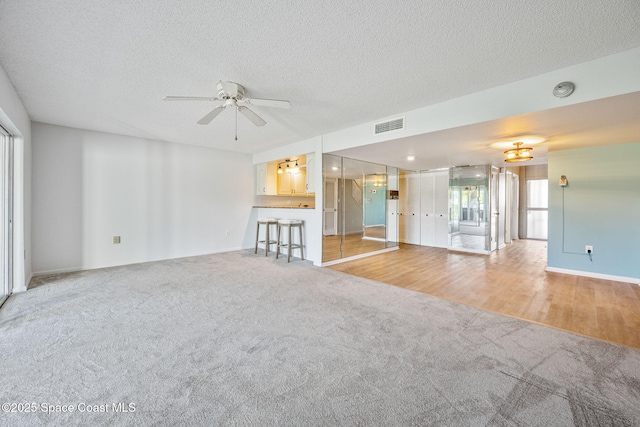 unfurnished living room with light carpet, ceiling fan, and a textured ceiling