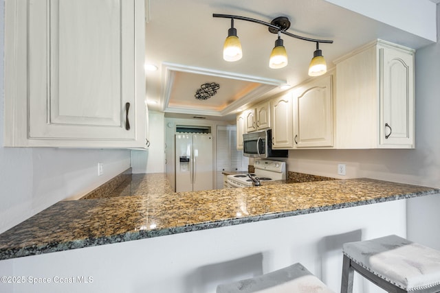 kitchen with white appliances, white cabinets, decorative light fixtures, a raised ceiling, and kitchen peninsula