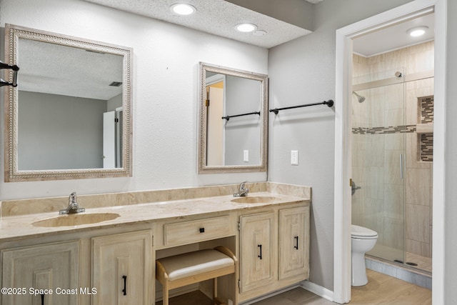 bathroom featuring toilet, vanity, an enclosed shower, and a textured ceiling