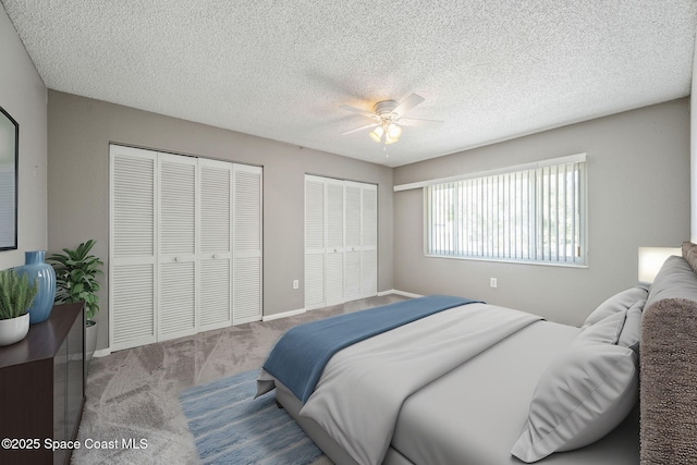 bedroom with ceiling fan, multiple closets, carpet floors, and a textured ceiling