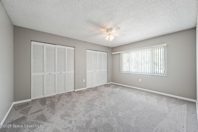 unfurnished bedroom featuring a textured ceiling, ceiling fan, two closets, and light colored carpet