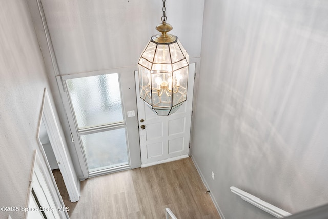 foyer entrance with light wood-type flooring, a towering ceiling, and a notable chandelier