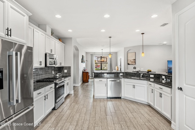 kitchen featuring light hardwood / wood-style floors, appliances with stainless steel finishes, white cabinetry, pendant lighting, and dark stone counters