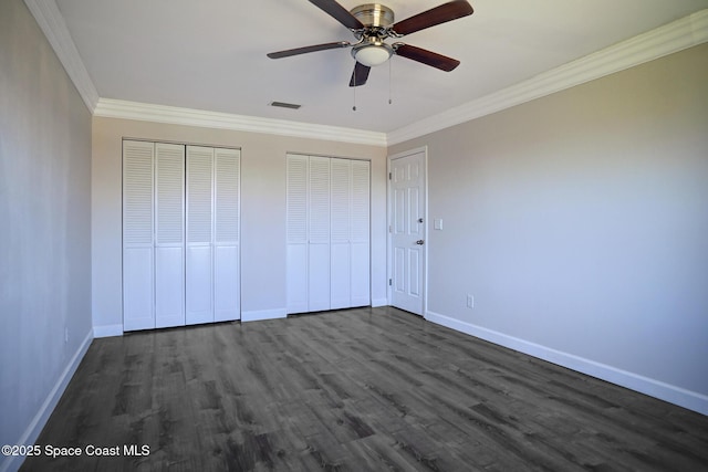 unfurnished bedroom featuring ceiling fan, dark hardwood / wood-style floors, two closets, and ornamental molding