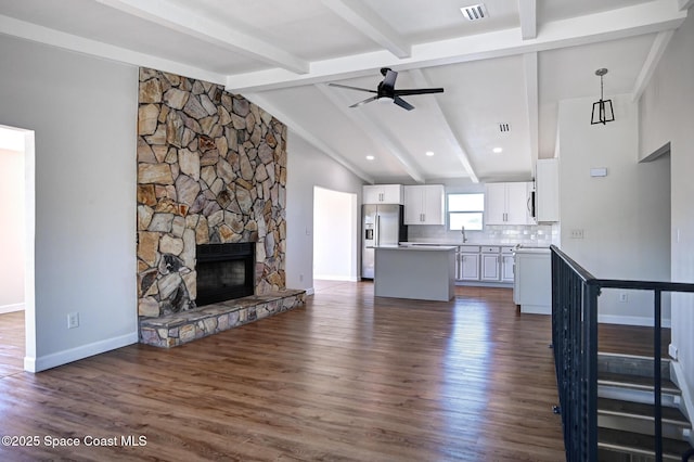 unfurnished living room with ceiling fan, sink, dark wood-type flooring, a stone fireplace, and vaulted ceiling with beams