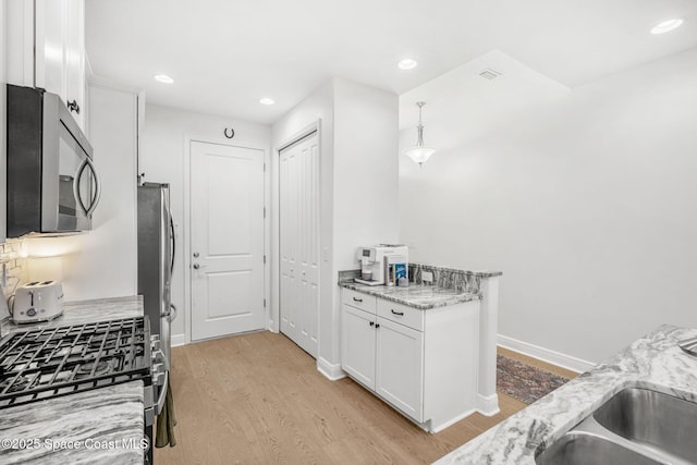 kitchen with sink, light stone counters, light hardwood / wood-style flooring, white cabinets, and appliances with stainless steel finishes