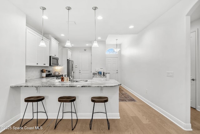 kitchen with white cabinetry, hanging light fixtures, stainless steel appliances, kitchen peninsula, and decorative backsplash