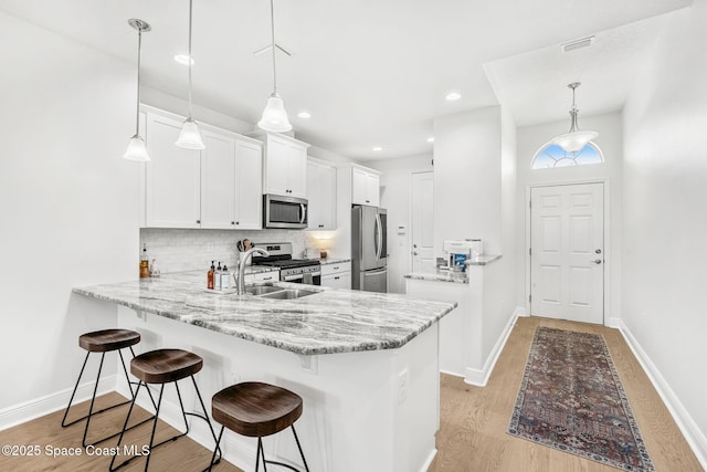 kitchen with kitchen peninsula, stainless steel appliances, white cabinetry, and hanging light fixtures