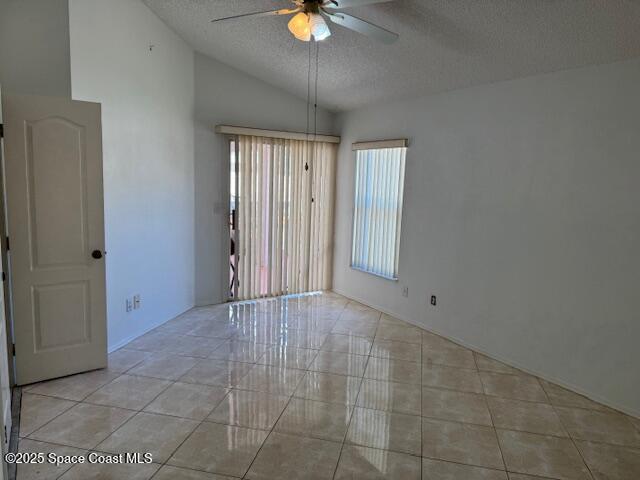 tiled empty room with ceiling fan, vaulted ceiling, and a textured ceiling