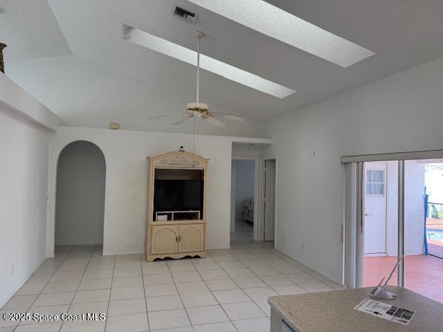 unfurnished living room featuring lofted ceiling with skylight, light tile patterned flooring, and ceiling fan