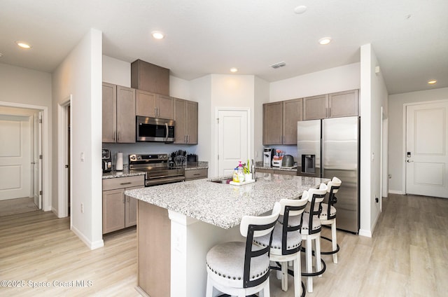 kitchen featuring a kitchen breakfast bar, light stone countertops, an island with sink, appliances with stainless steel finishes, and light hardwood / wood-style floors